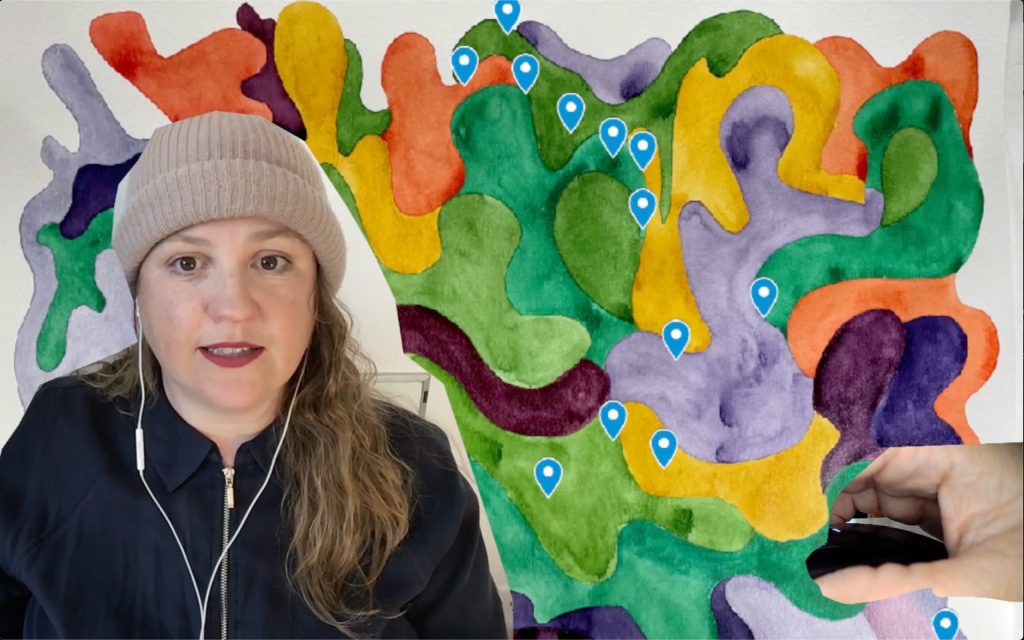 artist in front of painted shapes with map pins and a hand cutout